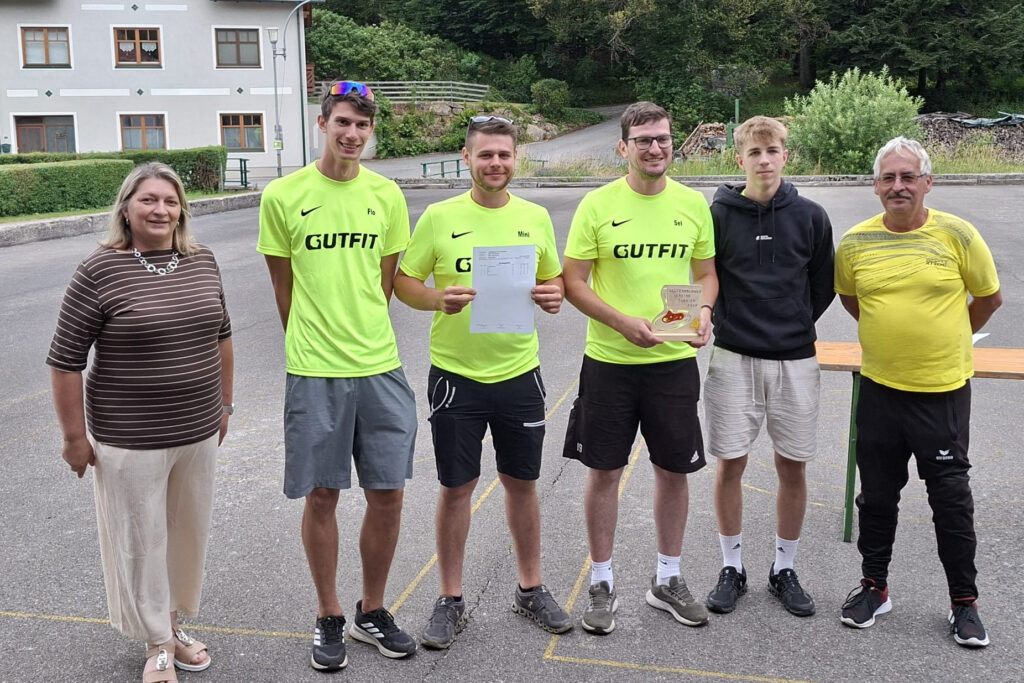 Siegerehrung in Österreich: Sportler mit Urkunde und Pokal vor Gebäude