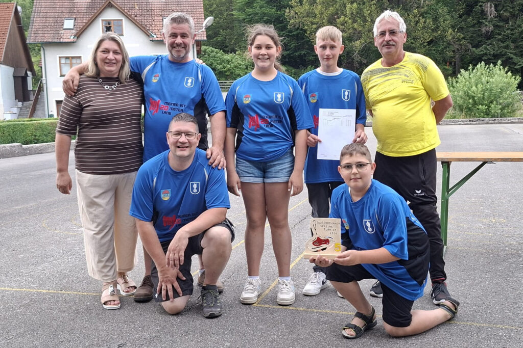 Zehn Personen im Freien mit einem Pokal und Urkunde, zwei Kinder halten die Trophäen.